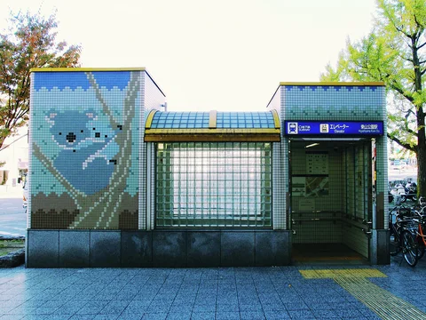 A small public restroom has a blue animal mosaic, glass-block panels, and an open entrance.