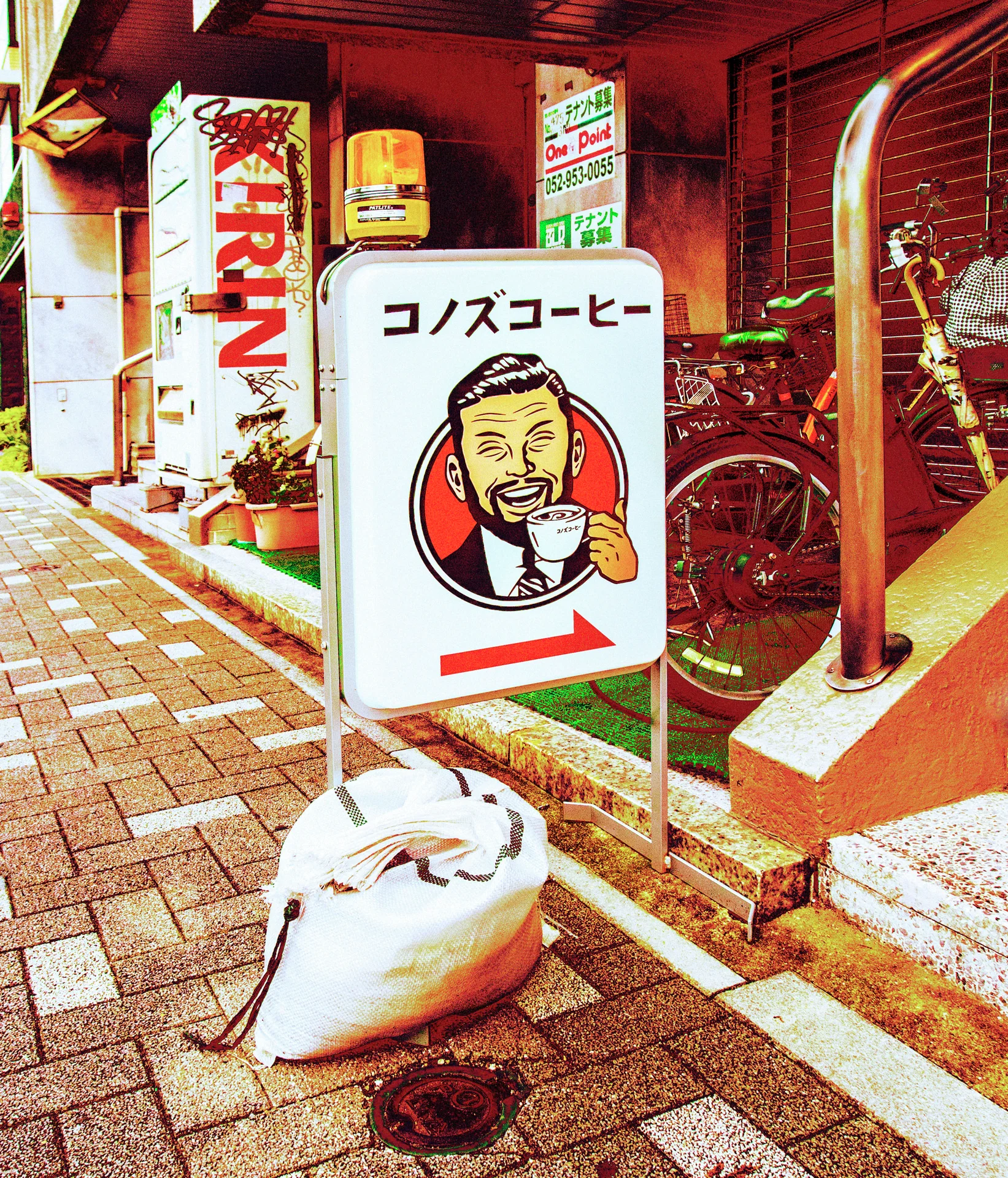 A cartoon coffee-drinker sign with a red arrow stands outside a shop beside a white sack.