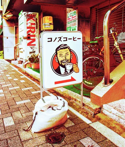 A cartoon coffee-drinker sign with a red arrow stands outside a shop beside a white sack.