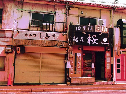 Faded restaurant signs span neighboring pink-toned storefronts with a closed shutter and a dark entrance.
