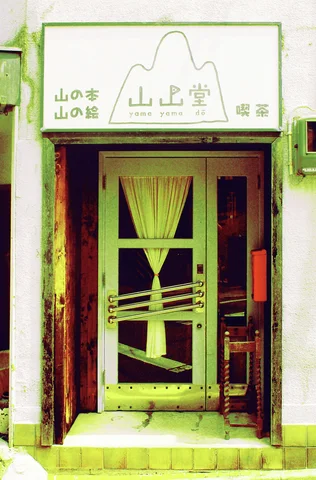 A narrow entrance has a curtained glass door beneath a pale sign with a simple mountain outline.