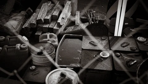 Plastic containers, weathered timber, and assorted scrap lie behind an out-of-focus wire fence.