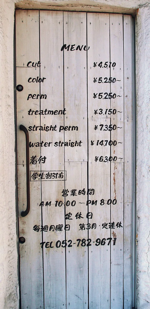 Handwritten salon services and prices cover a narrow white plank door with a long dark handle.