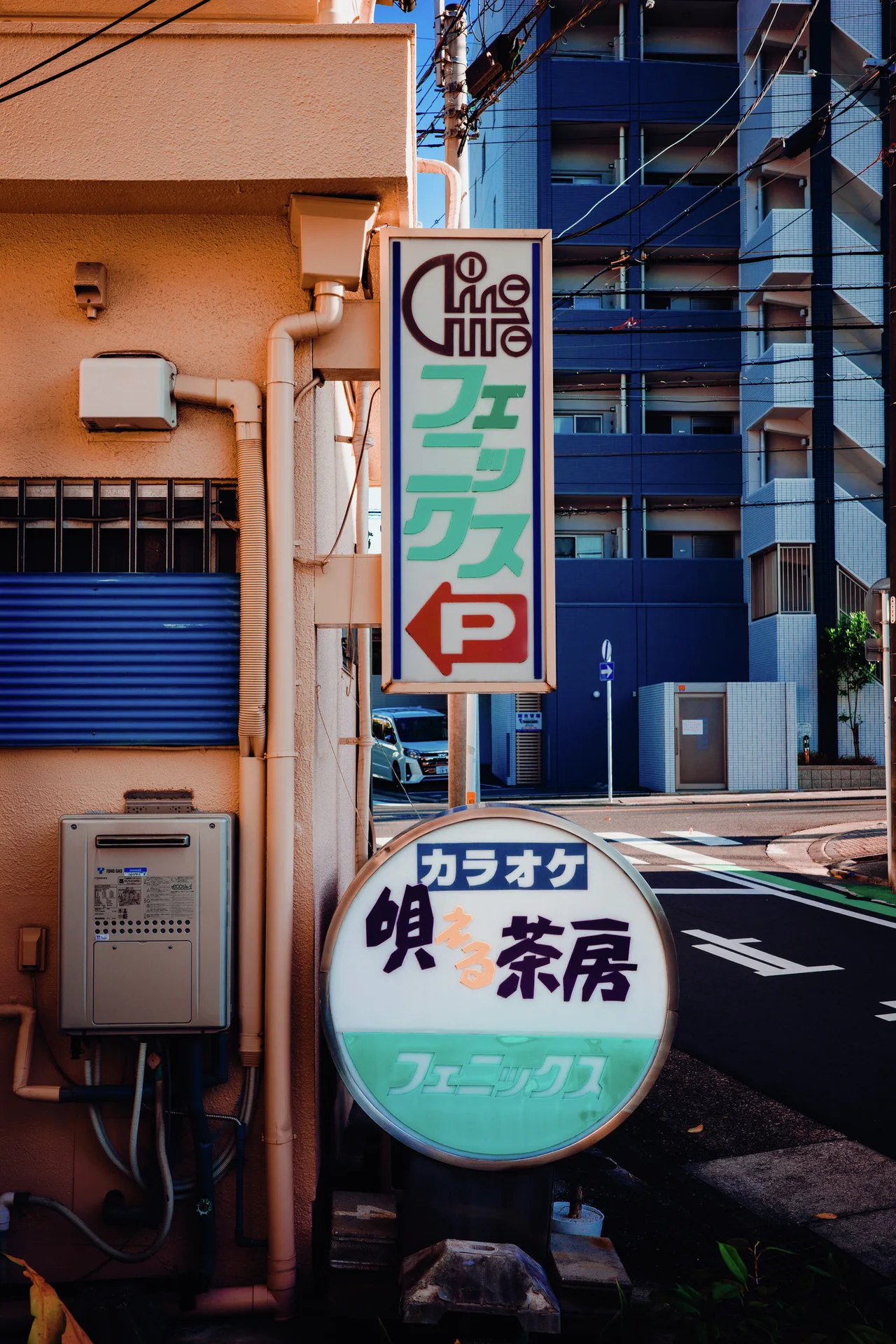 Vertical and round cafe signs project beside a pale building at a street corner.