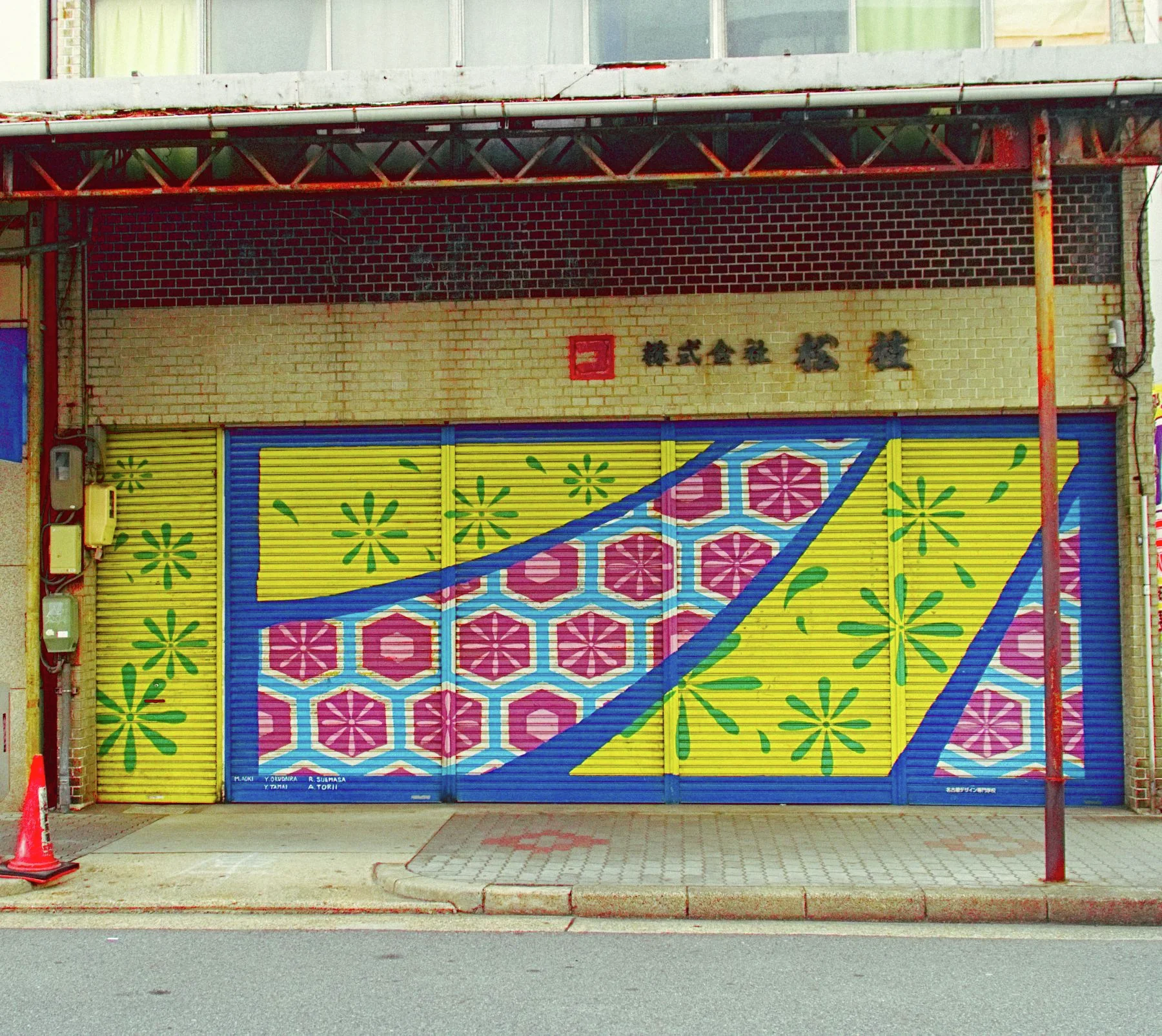 Yellow shop shutters carry green starbursts and diagonal bands of red and blue geometric patterns.