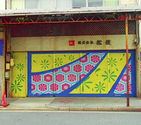 Yellow shop shutters carry green starbursts and diagonal bands of red and blue geometric patterns.