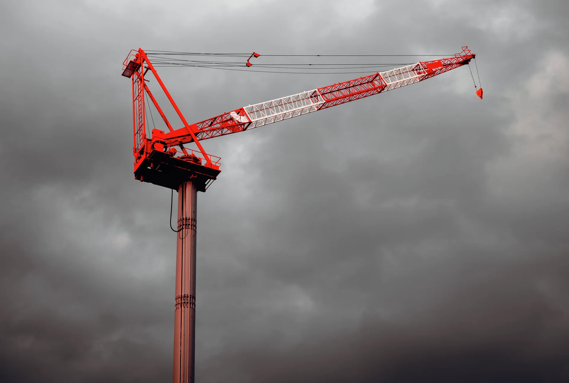 A red and white tower crane stretches across a dark cloudy sky.