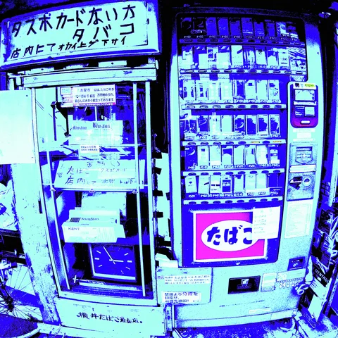 A cigarette vending machine stands beside an empty glass-fronted cabinet beneath Japanese signage in strong blue tones.