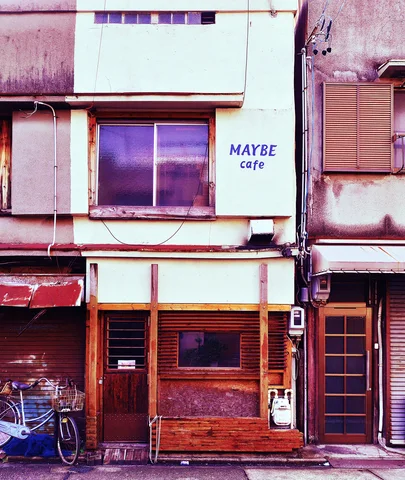 MAYBE cafe lettering marks a pale upper wall above a narrow red-brown wooden entrance.
