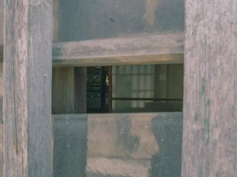 A narrow rectangular opening interrupts weathered wooden door panels, revealing a dark interior window.
