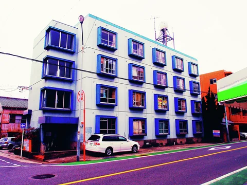 Rows of blue projecting window frames punctuate a white building beside a parked white car.
