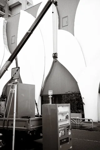 Large curved white panels rise beside a parking barrier and payment machine in black and white.