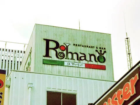 Decorative Romano restaurant lettering spans pale corrugated siding above a dark window and horizontal colored bands.