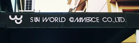 White Sun World Commerce lettering and a smiling emblem mark a dark horizontal sign between buildings.
