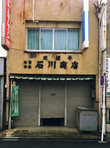 Closed gray shutters sit beneath a faded tan facade with blue windows and dark lettering.