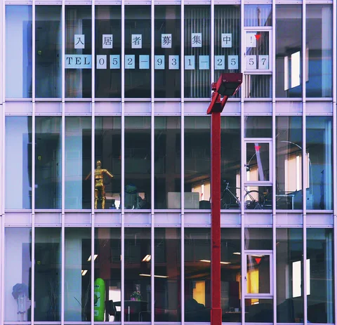 A grid of slender metal mullions divides windows revealing colored doors and furniture inside a multi-story building.