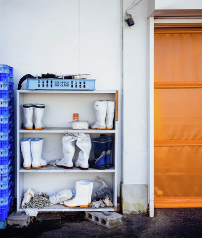 Pairs of tall white boots fill an open shelf beside blue crates and an orange sliding door.