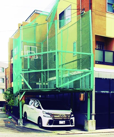 A tall green metal enclosure projects from a building above a parked white minivan.