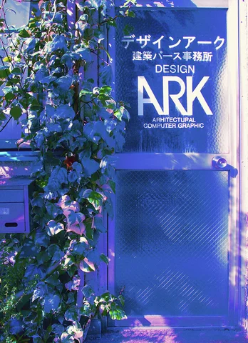 Leafy branches partly obscure a dark blue design office sign mounted above a matching door.