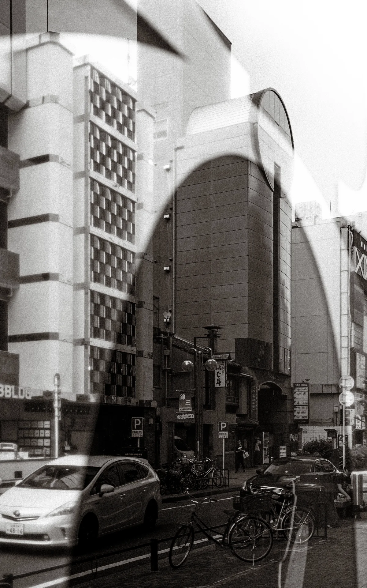 Reflected architectural curves overlap an urban street with cars and bicycles in a black and white view.