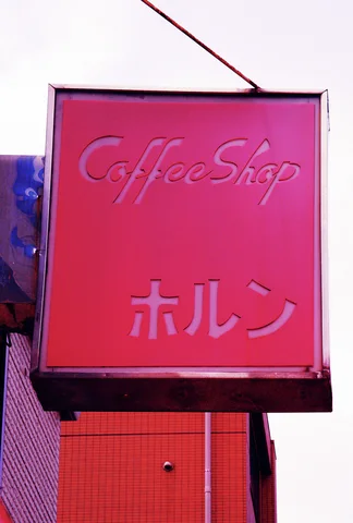 Pale cursive Coffee Shop lettering marks a faded pink projecting sign within a dark metal frame.