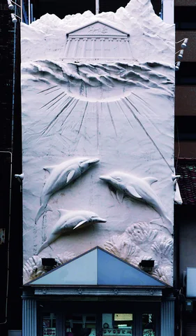 Raised dolphin shapes decorate a tall narrow wall above a small entrance with a blue triangular canopy.
