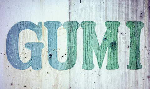 Large faded blue-green letters mark a pale corrugated wall streaked with weathering and dark spots.