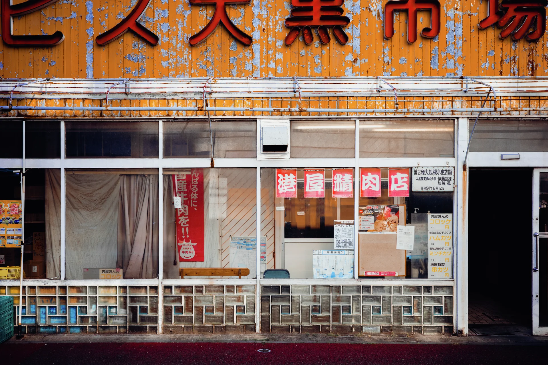 Large red Japanese characters crown a weathered orange storefront above broad glass windows and white railings.