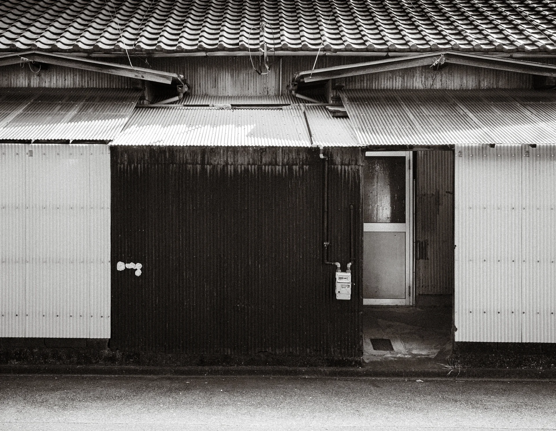 Corrugated awnings project beneath a tiled roof above a dark wooden facade in black and white.