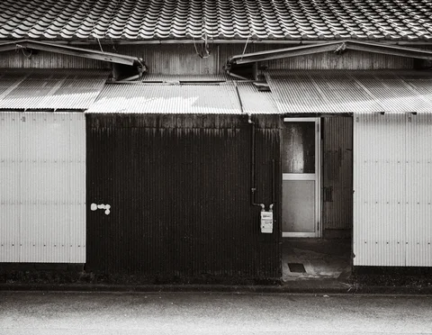 Corrugated awnings project beneath a tiled roof above a dark wooden facade in black and white.