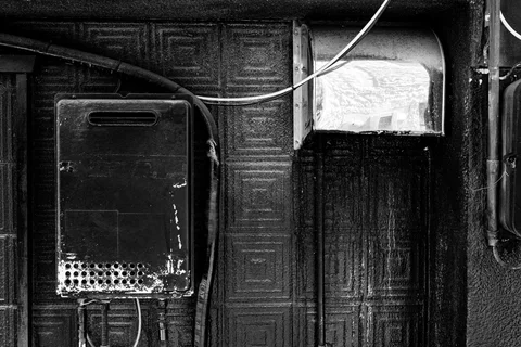 Black and white wall fixtures include a weathered rectangular box and a curved vent beneath looping cables.
