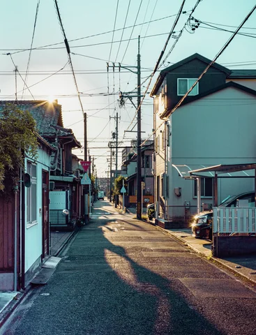Long shadows stretch along a narrow residential lane beneath a web of overhead wires.