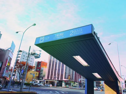 A long station entrance canopy with a blue sign extends diagonally above a busy urban street.