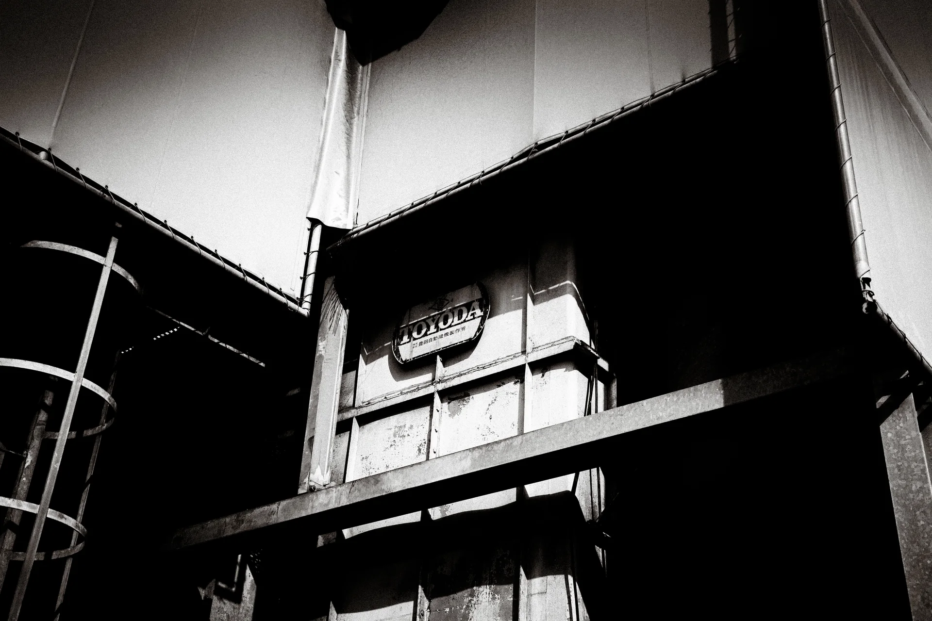 Angular pale roof panels frame a weathered tower and dark horizontal beam in black and white.