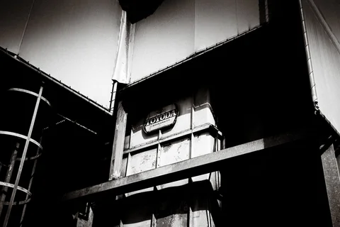 Angular pale roof panels frame a weathered tower and dark horizontal beam in black and white.