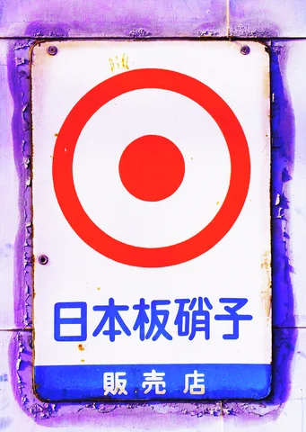 A bold red target symbol fills a white metal sign above blue Japanese lettering.