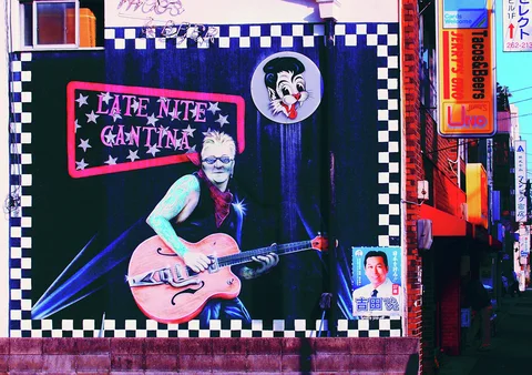 A mural of a guitarist fills a dark wall panel bordered by black-and-white checks and small posters.