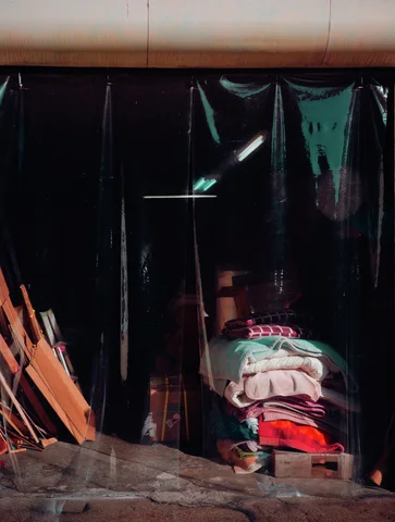 Dark translucent curtains cover a cluttered entrance with stacked fabric and leaning wooden boards.