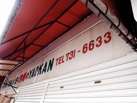 Dark and red lettering runs above closed white shutters beneath the metal supports of a red awning.