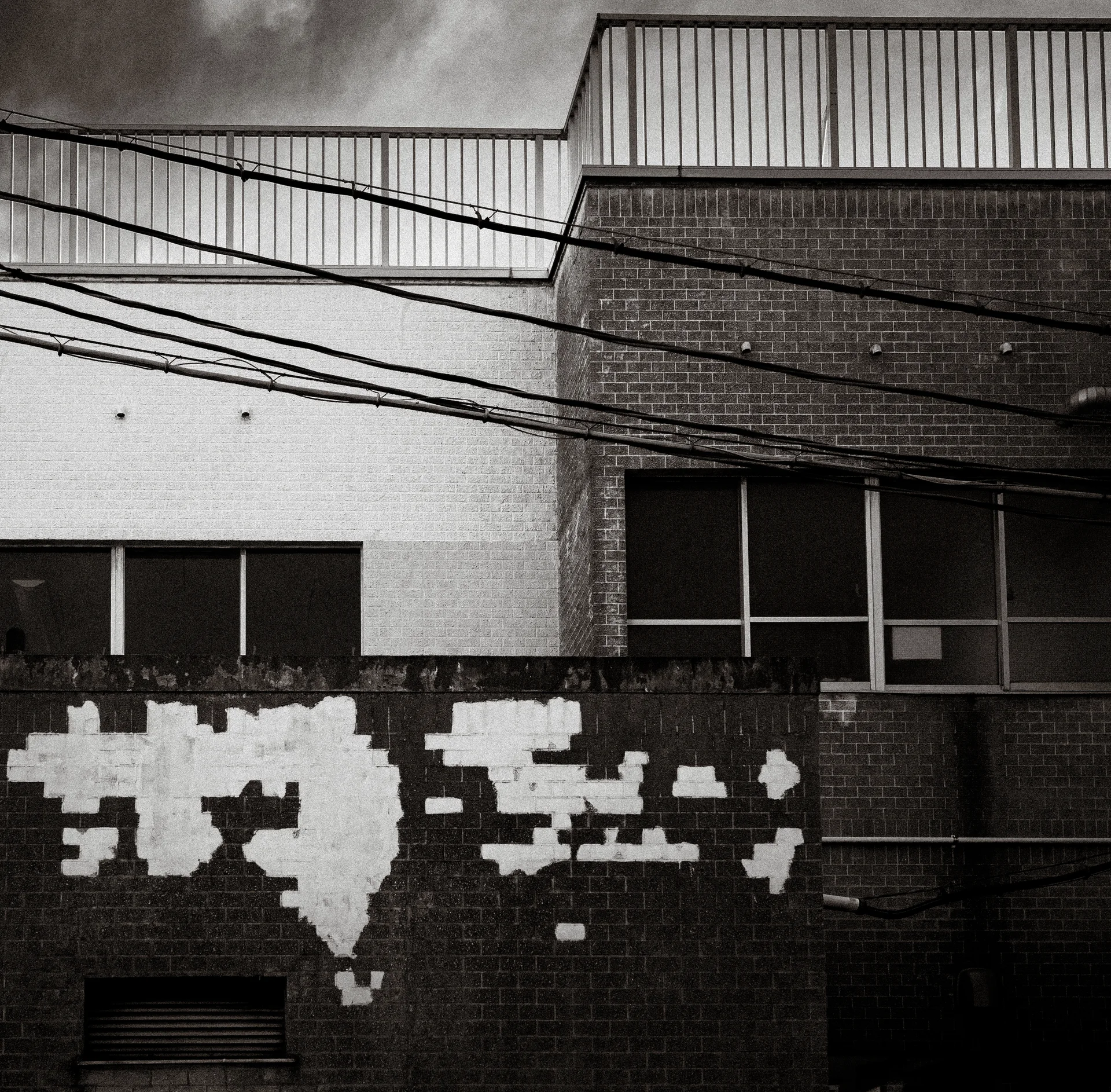 Peeling pale paint forms irregular patches across a brick facade beneath crossing cables in black and white.