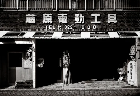 Raised white lettering spans a brick workshop facade above a deeply shadowed opening in monochrome.