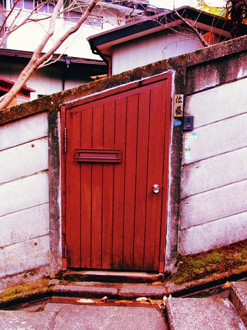 A narrow red wooden door with a mail slot is set into a pale block wall.