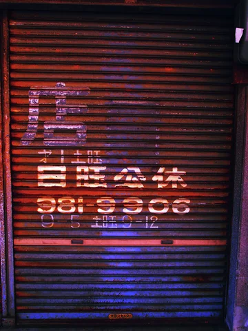 Faded white lettering spans dark red closed shutters with a blue lower section.