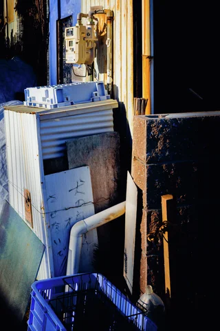 Small containers rest on weathered exterior equipment beside pipes and a blue plastic crate.