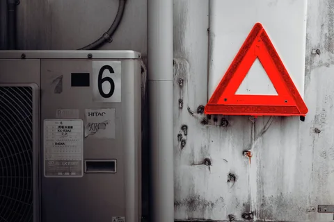 A bright red triangular reflector hangs on a pale stained wall beside an air conditioner marked 6.