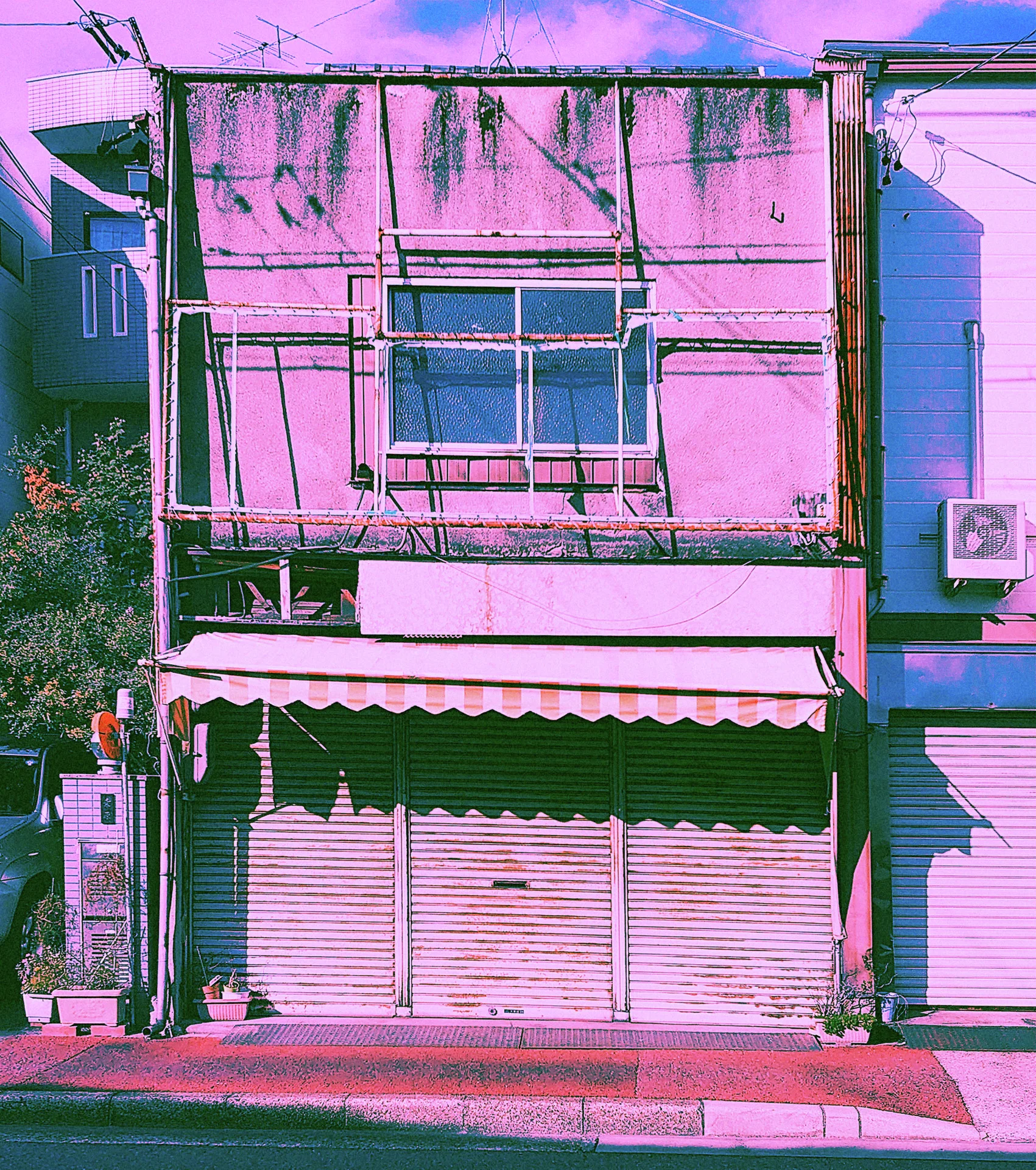 A weathered pink storefront has stained upper walls and closed shutters beneath a pale awning.