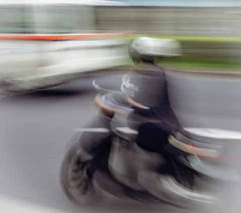 A helmeted scooter rider blurs across the foreground as a pale bus streaks behind.
