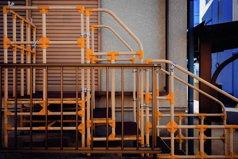 Orange joints punctuate a dense arrangement of pale metal stair railings beside closed shutters.