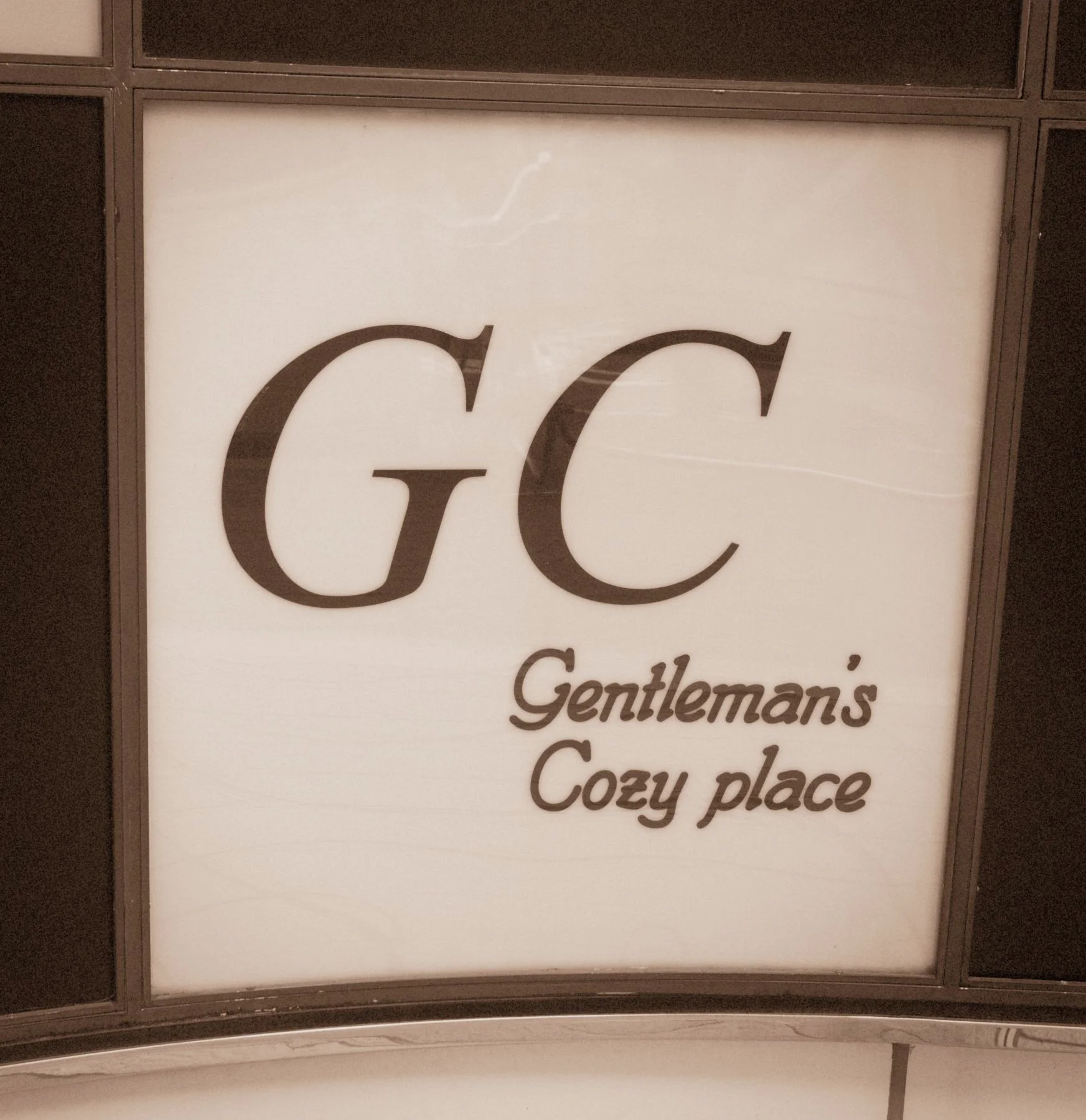 Large GC initials and smaller Gentleman窶冱 Cozy place lettering fill a pale framed sign panel.