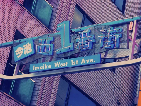 A turquoise street arch with raised lettering crosses before a brick building with dark windows.